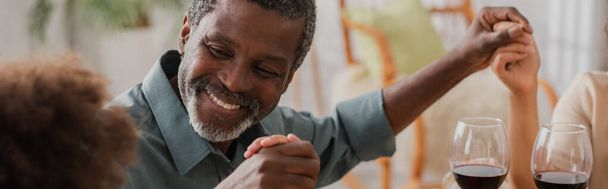 cheerful african american man holding hands with family during pray on thanksgiving dinner, banner - 写真・画像