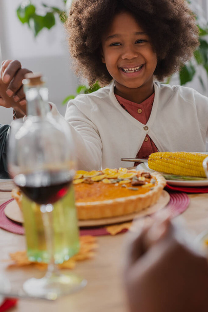 glimlachend Afrikaans Amerikaans meisje hand in hand met opa tijdens het bidden tijdens dankzegging diner - Foto, afbeelding