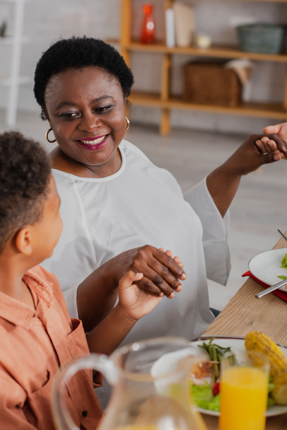 happy african american woman holding hands with grandson and daughter while praying before thanksgiving dinner - Foto, Imagen