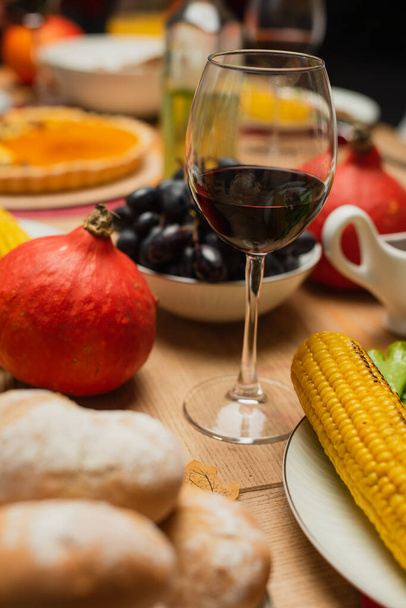 glas rode wijn bij hele pompoen, gegrilde maïs en verse druiven op tafel geserveerd met dankdag - Foto, afbeelding