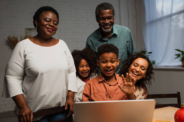 excited african american boy waving hand during video call near family - Photo, Image