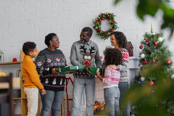 african american kids presenting christmas gifts to pleased grandparents near mother - Foto, imagen