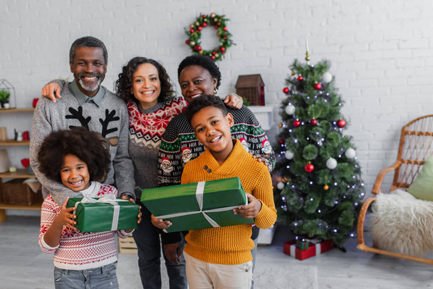 joyful african american kids with christmas gifts looking at camera near mother and grandparents - Foto, immagini