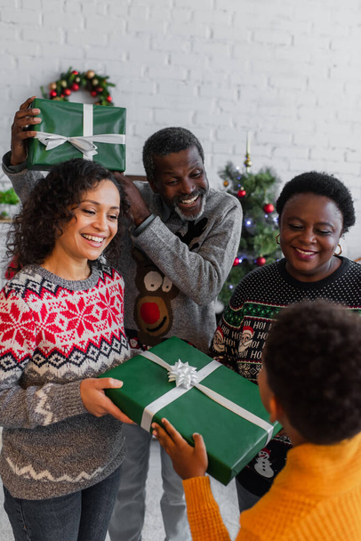 happy african american family holding christmas gifts near blurred boy at home - 写真・画像