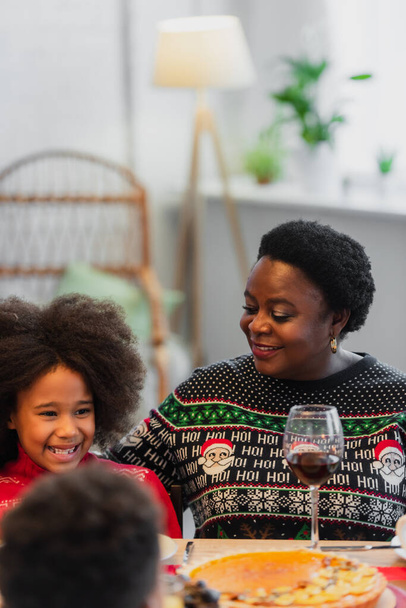cheerful african american girl smiling near granny and blurred brother during christmas dinner - 写真・画像