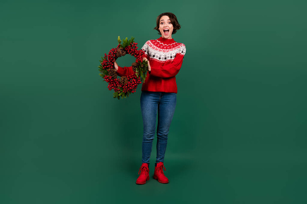 Full length body size view of attractive cheerful amazed girl holding festal eve wreath isolated over green color background - 写真・画像