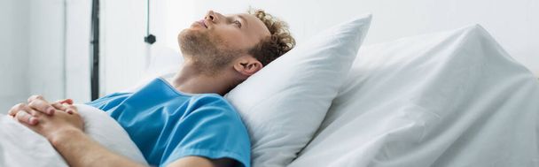 curly young patient with clenched hands lying on hospital bed, banner - Фото, изображение