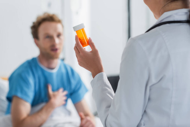 doctor in white coat holding bottle with medication near blurred patient  - Foto, imagen