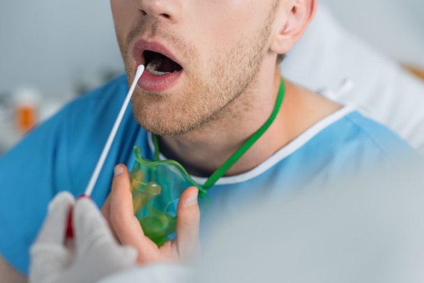 przycięty widok lekarza trzymającego wymaz w pobliżu pacjenta z otwartymi ustami  - Zdjęcie, obraz