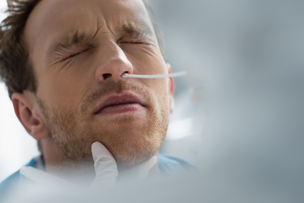 orvos latex kesztyű gazdaság tampon orra mellett a beteg csukott szemmel, miközben csinál pcr teszt - Fotó, kép