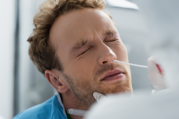medico in guanto di lattice che tiene tampone vicino al naso del paziente riccio con gli occhi chiusi durante l'esecuzione del test del pcr nasale - Foto, immagini