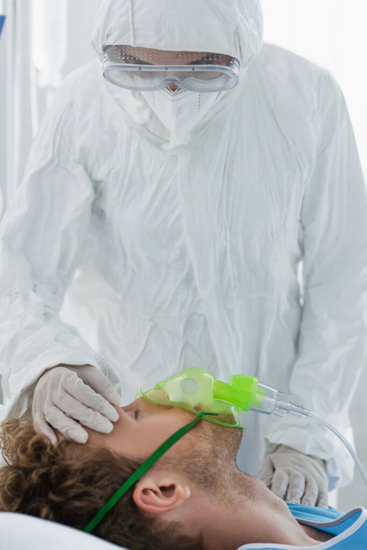 médico en equipo de protección personal que examina al paciente con máscara de oxígeno  - Foto, Imagen