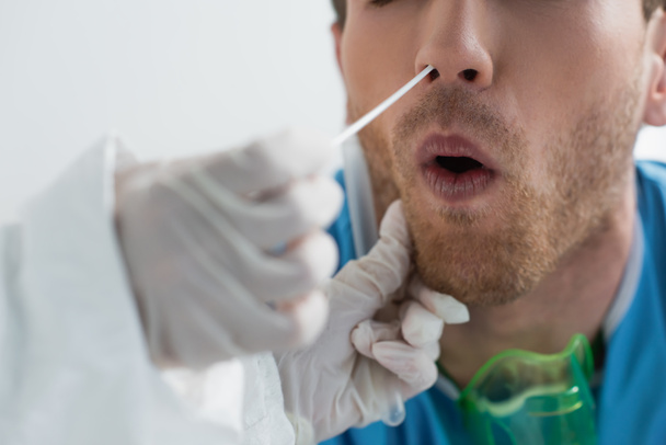 μερική άποψη του γιατρού σε γάντια λατέξ κρατώντας μάκτρο κοντά στη μύτη του σγουρά ασθενή, ενώ κάνει ρινική δοκιμή pcr - Φωτογραφία, εικόνα