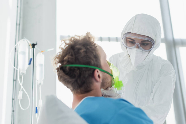 médico en equipo de protección personal y gafas que examinan al paciente con máscara de oxígeno en el hospital  - Foto, imagen