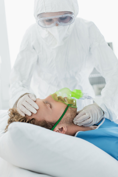 medico in tuta hazmat e occhiali esaminando il paziente in maschera di ossigeno in ospedale  - Foto, immagini