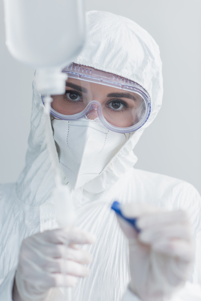 doctor in hazmat suit and goggles holding catheter on drop counter - Φωτογραφία, εικόνα