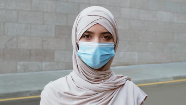 Junge muslimische Frau mit Hijab und medizinischer Schutzmaske schaut in die Kamera im Freien, Kamerafahrt - Filmmaterial, Video