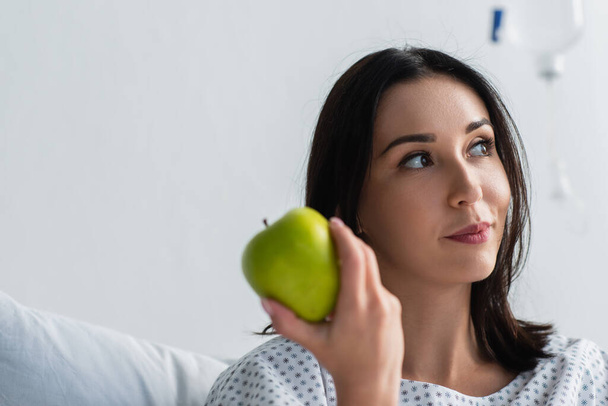 brunette woman holding fresh apple in hospital  - Foto, Bild
