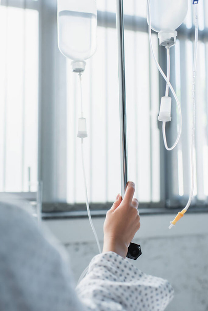 bijgesneden zicht van zieke vrouw hand in hand op drop teller met intraveneuze therapie flessen - Foto, afbeelding