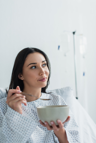 pensive patient holding spoon and bowl with breakfast in hospital  - Fotoğraf, Görsel