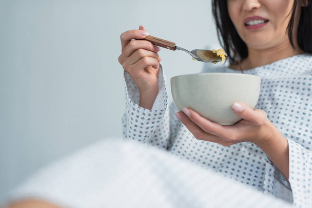 cropped view of disgusted woman holding spoon with corn flakes and bowl in hospital  - Foto, Imagem