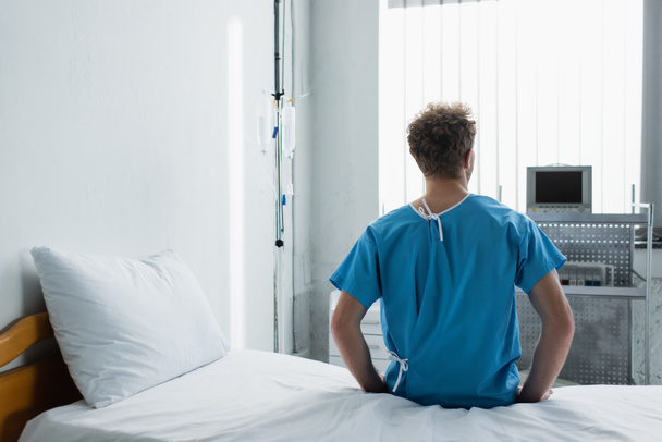 Rückansicht des lockigen Mannes auf dem Krankenhausbett  - Foto, Bild