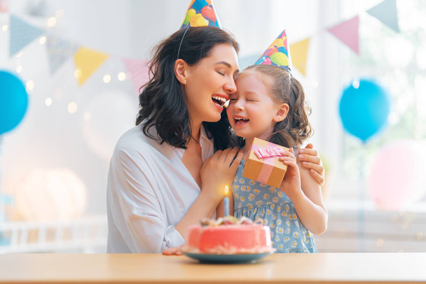 The kid is blowing out the candles on the cake. Mother and daughter are celebrating birthday. - Φωτογραφία, εικόνα