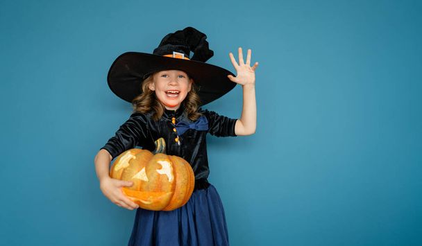 Happy Halloween! Cute little laughing girl in witch costume on blue wall background.  - Фото, изображение
