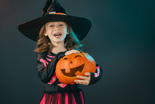 Happy Halloween! Cute little laughing girl in witch costume on black wall background.  - Photo, image