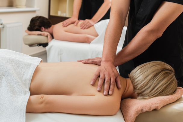 Masseur faire massage sur les épaules de la jeune femme près de collègue et homme dans le centre de spa  - Photo, image