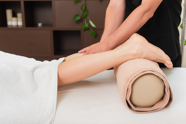 Vista cortada do massagista fazendo massagem na perna da jovem no centro de spa  - Foto, Imagem