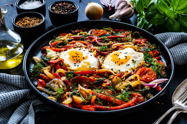 Shakshuka - fried eggs with vegetables on black wooden table  - Foto, immagini
