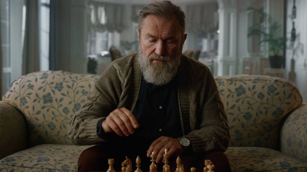 Idősebb férfi sakkozik egyedül a klasszikus nappaliban. Összpontosított, érett úriember  - Fotó, kép