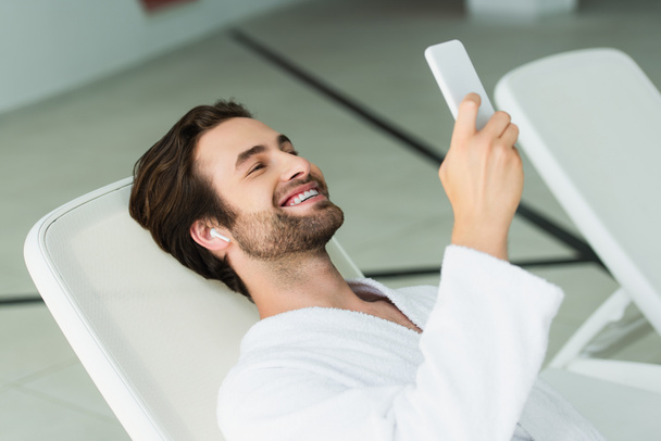 Smiling man in earphone using smartphone in spa center  - Photo, Image