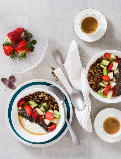 breakfast with granola, yogurt, fresh fruit, chia seeds, maple syrup and berries in plates on the table - Foto, afbeelding