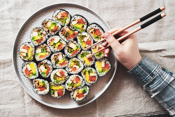 vegan sushi with tofu and avocado on a plate on a linen napkin. female hand - Fotografie, Obrázek