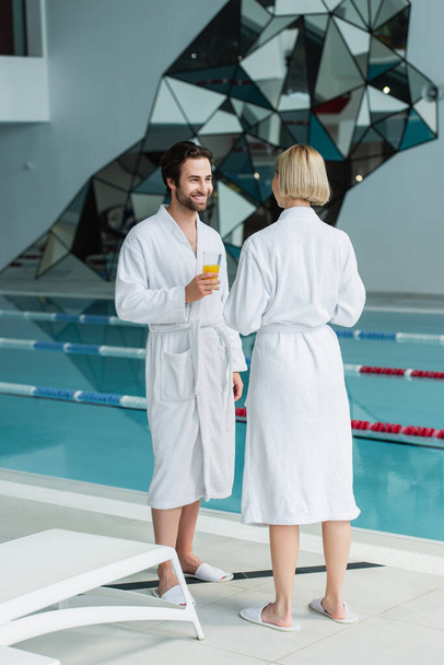 Cheerful man with orange juice talking with girlfriend in spa center  - Photo, Image