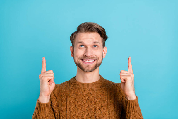 Photo of attractive pretty young guy dressed knit sweater smiling looking pointing up empty space isolated blue color background - Fotografie, Obrázek