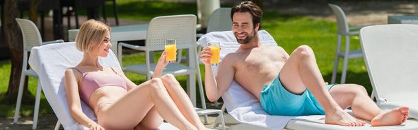 Pareja sonriente sosteniendo jugo de naranja en tumbonas en el resort, pancarta  - Foto, imagen