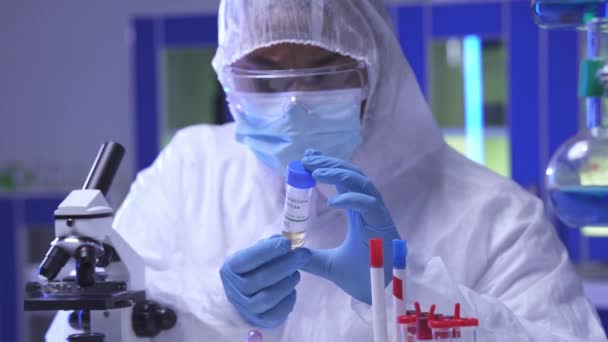 Indický vědec v lékařské masce držení vakcíny v blízkosti mikroskopu a zkumavky  - Záběry, video
