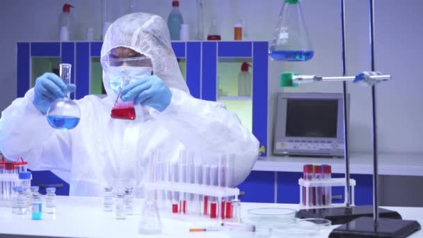 ハズマットスーツのインドの科学者は、実験室のフラスコでサンプルを扱う  - 映像、動画