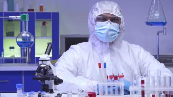 Індійський вчений в костюмі з небезпекою біля мікроскопа і тестових труб в лабораторії.  - Кадри, відео