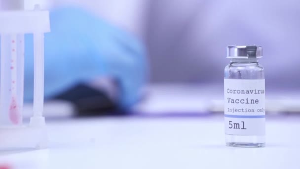 Обрезанный вид ученого, выставляющего коронавирусную вакцину на стол в лаборатории  - Кадры, видео
