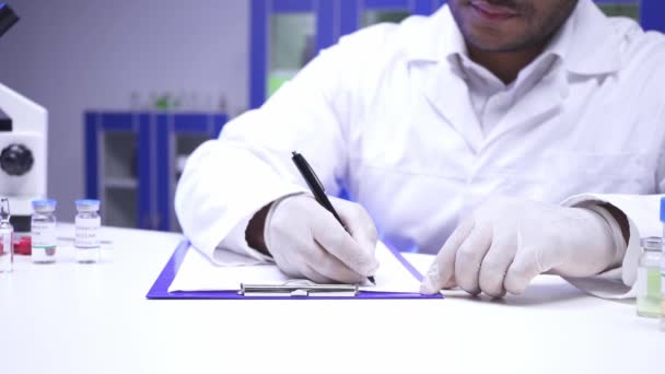 Widok naukowca piszącego na schowku i trzymającego słoik ze szczepionką  - Materiał filmowy, wideo