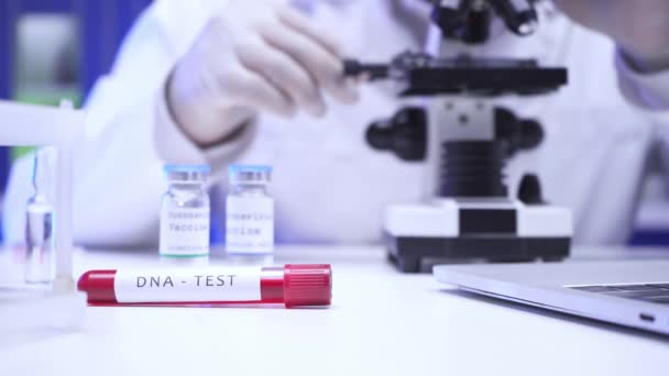 Laboratuvarda bilim adamı ve dizüstü bilgisayarın yanında DNA harfleri bulunan test tüpü görüntüsü.  - Video, Çekim
