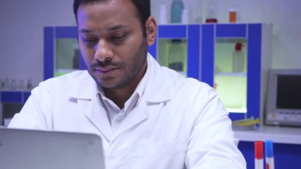 Indischer Wissenschaftler mit Laptop und Haltglas mit Impfstoff im Labor  - Filmmaterial, Video