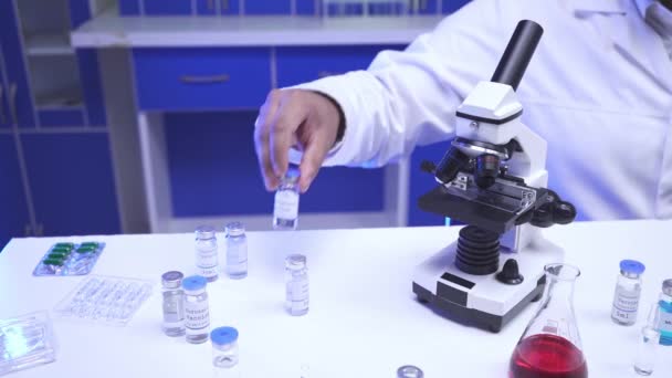 Vista ritagliata dello scienziato che lavora con vaccino, laptop e microscopio in laboratorio  - Filmati, video