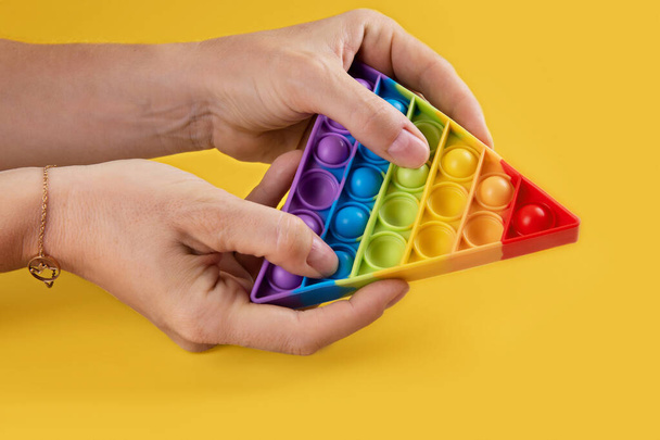 Hans hembra que utiliza antiestrés juguete popit arco iris para niños y adultos sobre un fondo amarillo. Flexible juguete antiestrés sensorial pop forma redonda, espacio de copia - Foto, imagen