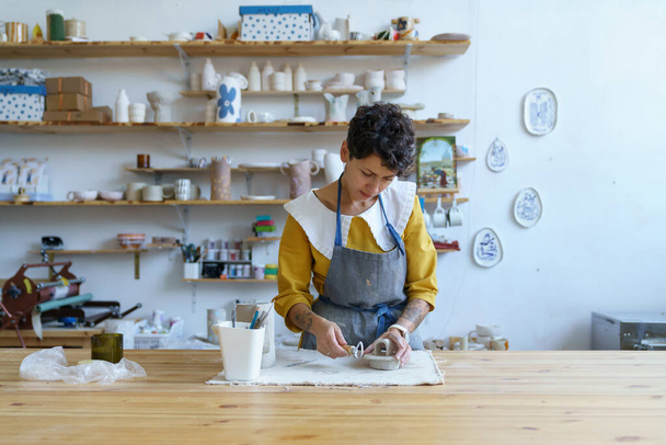 Çömlek atölyesindeki yaratıcı süreç: genç sanatçı kız çömlekçi için ham çamurdan heykel modelliyor - Fotoğraf, Görsel