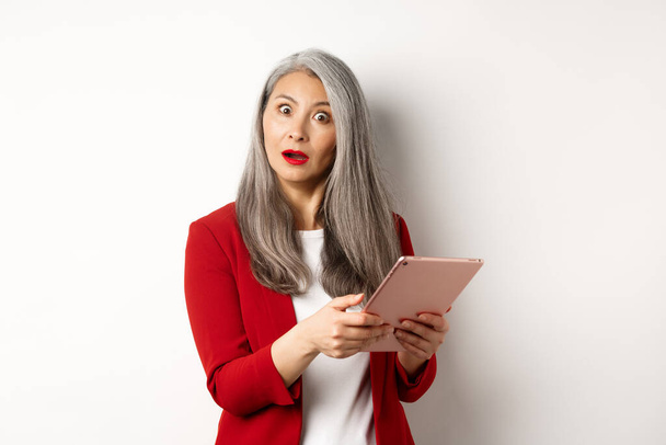 Obchod. Překvapená asijské podnikatelka hledá dojem po přečtení něco na digitálním tabletu, stojící nad bílým pozadím - Fotografie, Obrázek